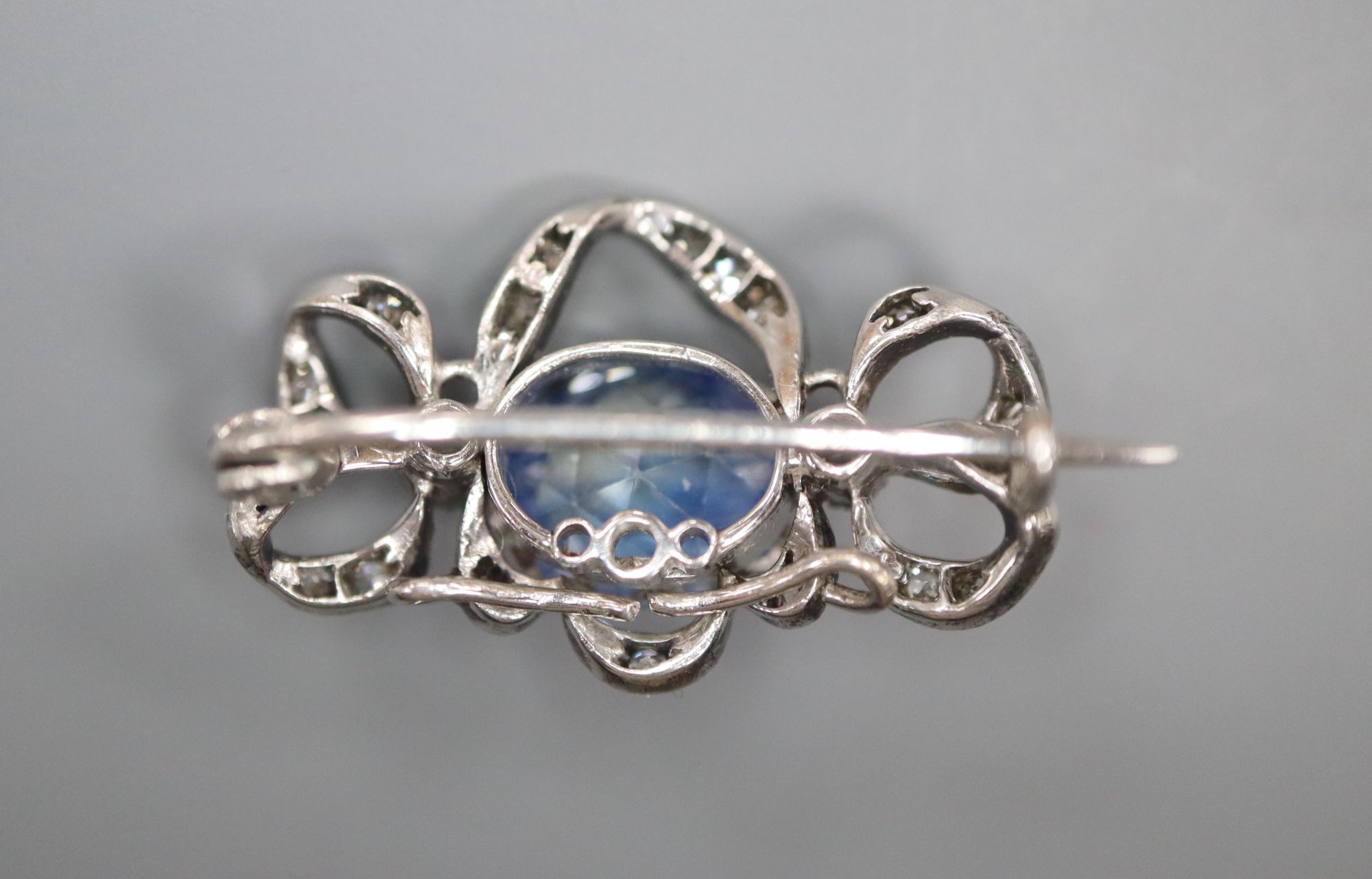An early 20th century white metal, fancy cut sapphire and diamond chip set scroll pendant brooch, 19mm, gross 4.4 grams.